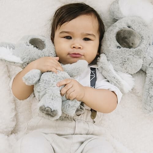 Baby holding two plush koala toys.