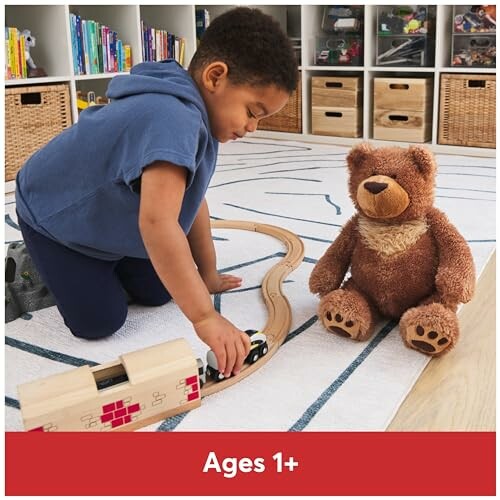 Child playing with a toy train set and teddy bear on the floor.