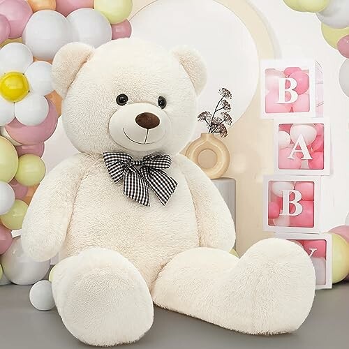 Large white teddy bear with a bow tie sitting next to baby blocks in pastel-themed setting.