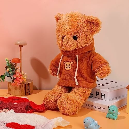 Teddy bear in a brown hoodie sitting on a table with decorative items.